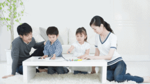A family sitting on a white floor playing with their children under the guidance of a mental health professional.
